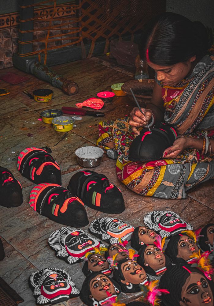An artisan skillfully paints traditional Indian masks, showcasing vibrant cultural artistry.