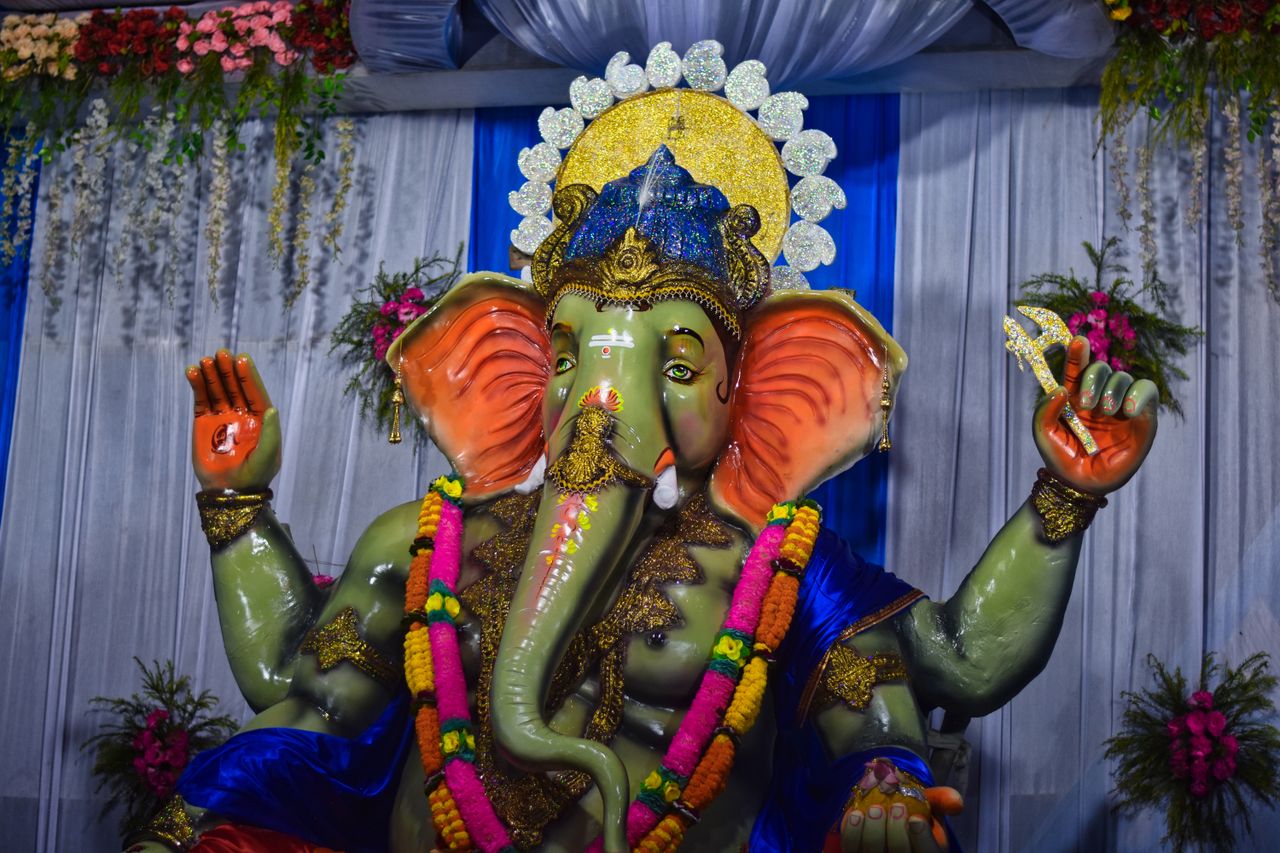 Colorful Ganesha statue adorned with flowers and festive decorations, captured indoors.