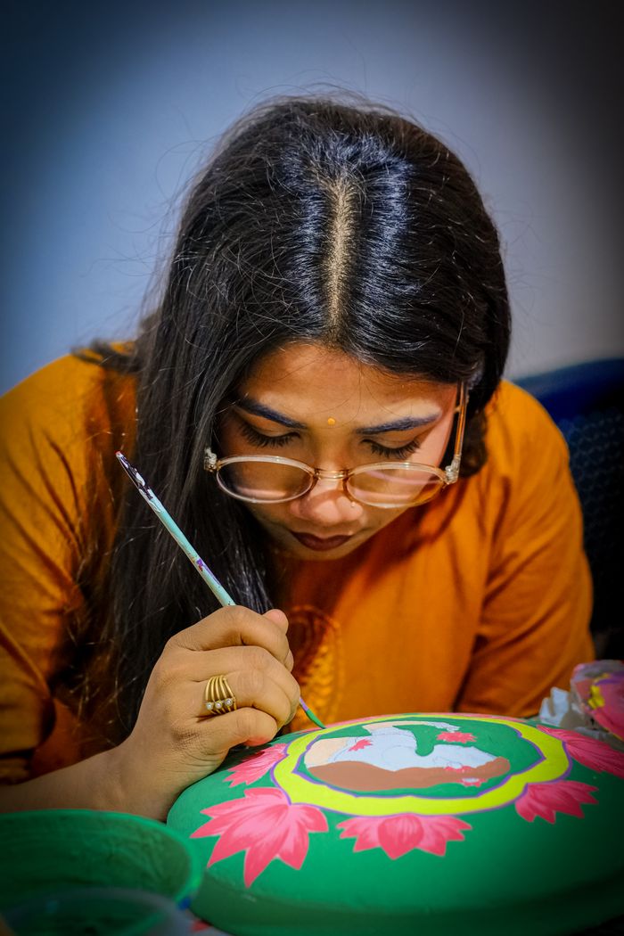 Young woman with glasses painting on a colorful canvas indoors, showcasing creativity.