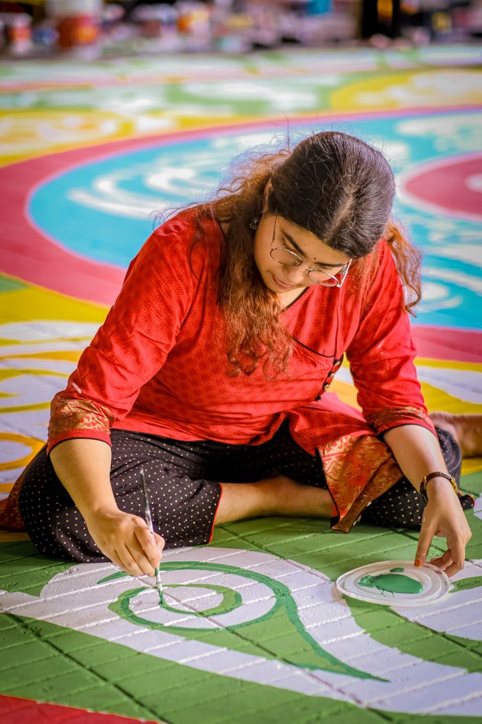 Woman in red crafting an intricate Rangoli design with vibrant colors.